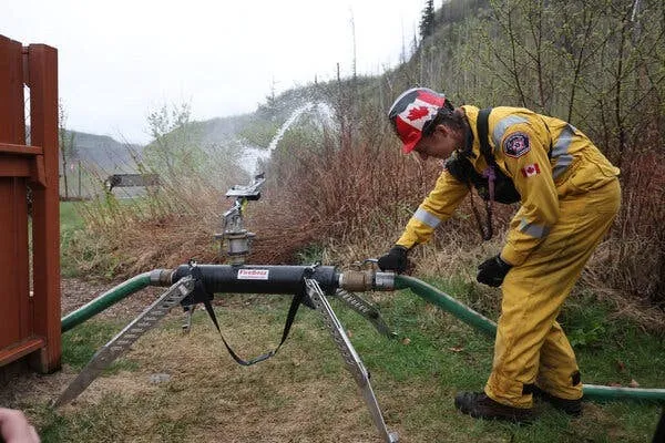 Firefighter in yellow turnout gear connecting a hose to a FireBozz unit spraying beside a building
